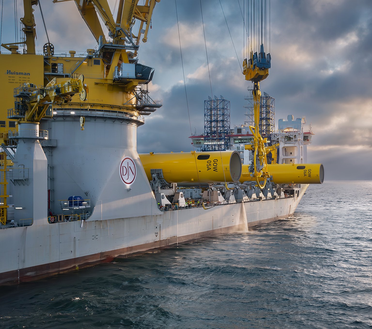 Installation vessel positions yellow monopile at sea under sunrise sky