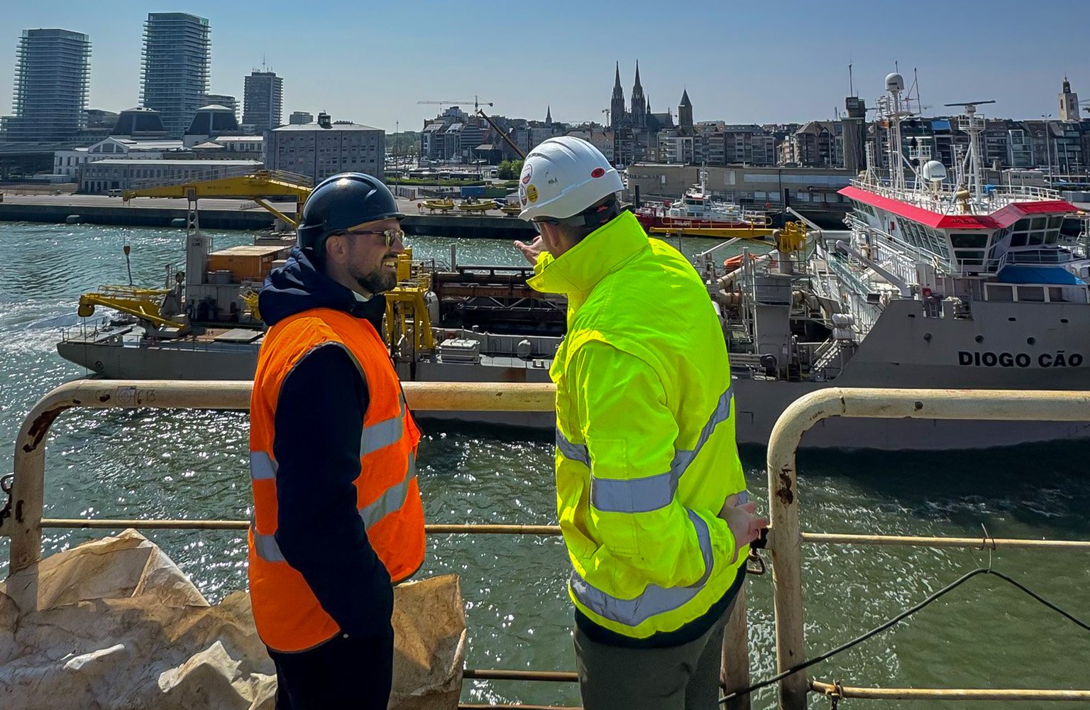 Sales Consultant and Engineer in safety gear meet dockside near Jan De Nul vessels